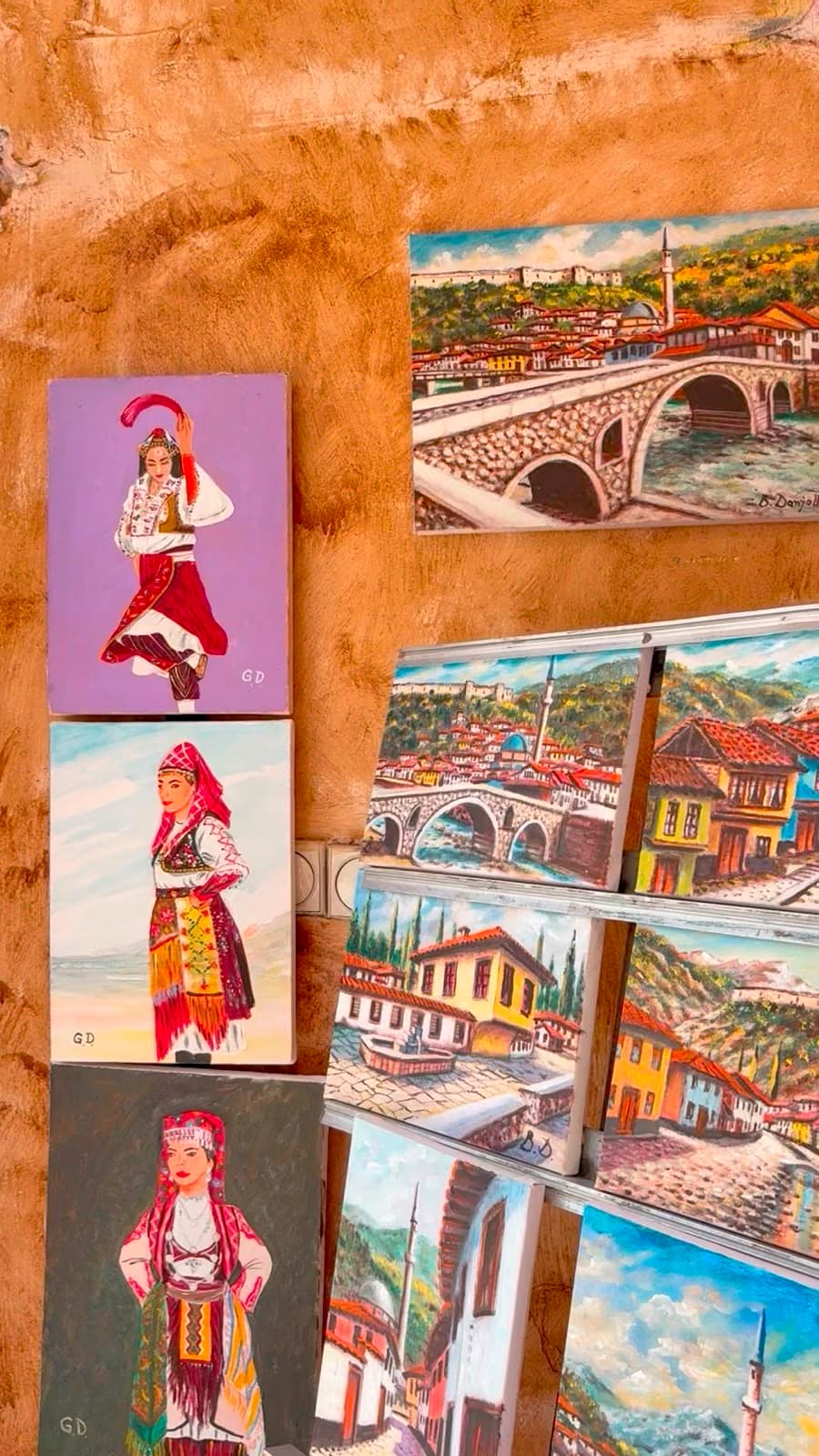 Paintings of Kosova landscapes and traditional dress displayed in an artist's studio
