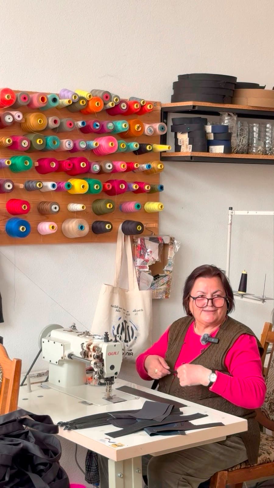 A seamstress seated at an industrial sewing machine beneath a wall of colourful thread