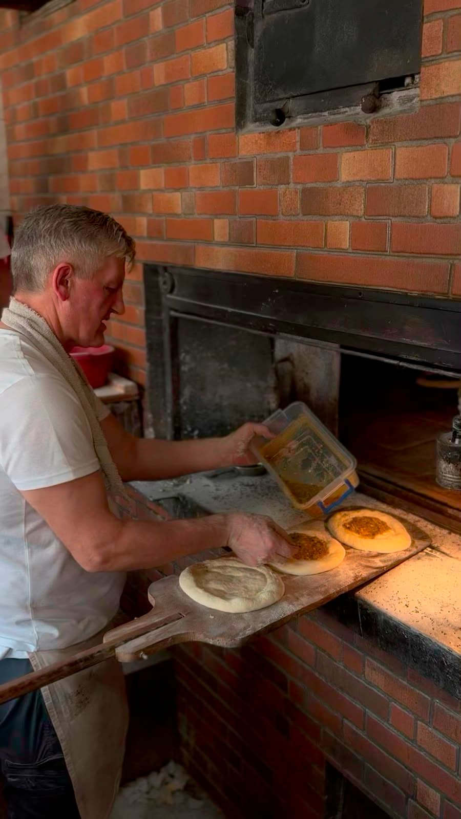 A baker sliding flatbreads into a brick wood-fired oven